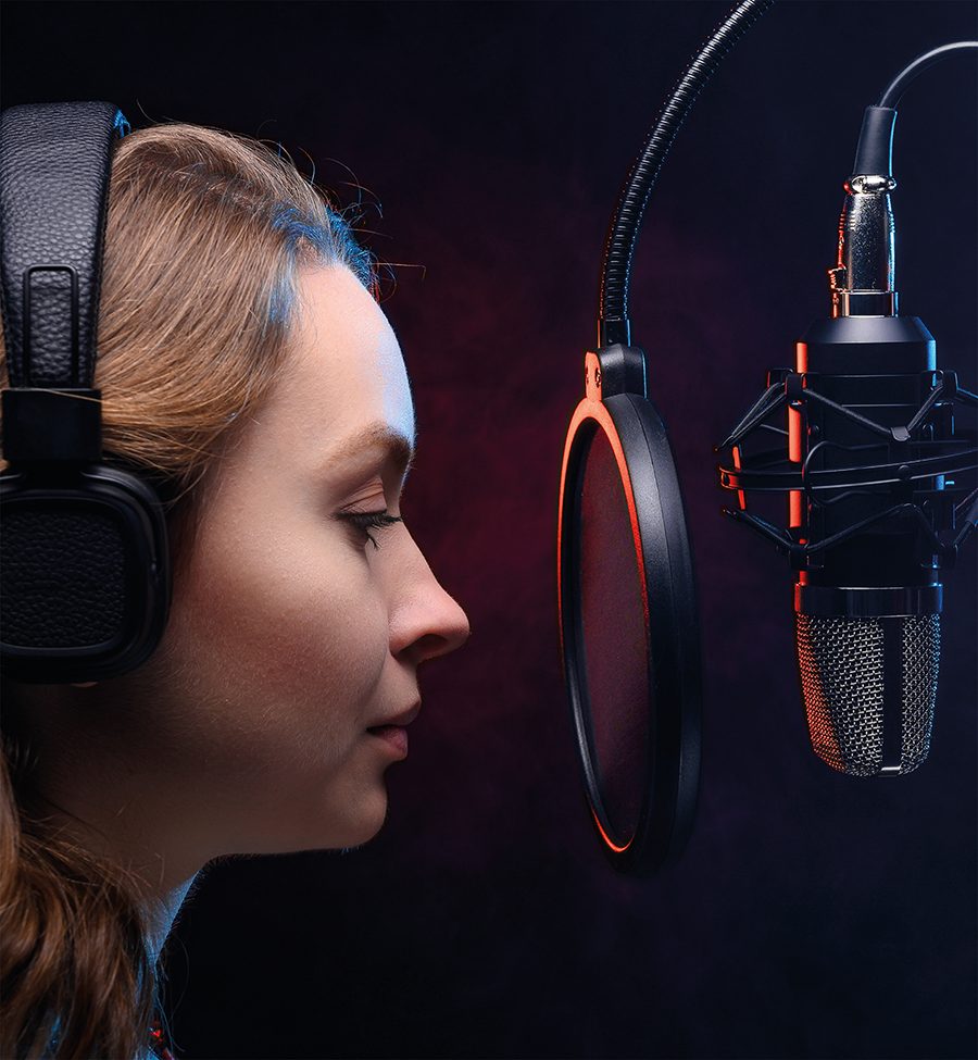 Comédienne enregistrant un message audio au micro, casque sur les oreilles, en studio